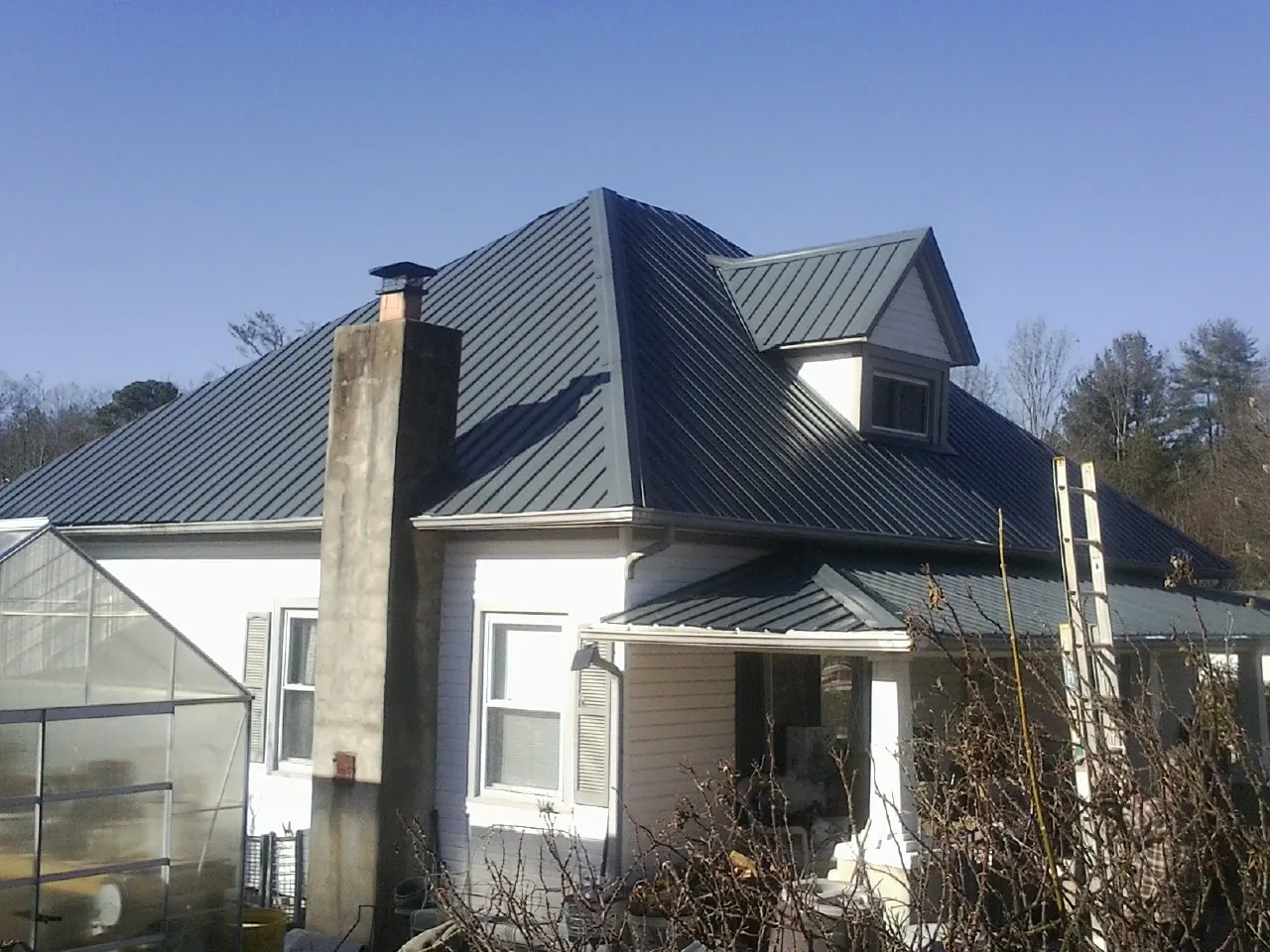 Dark blue standing seam metal roof on a white farmhouse with dormer — Slate & Tile Roof Repair by Roofing Brothers in Pfafftown