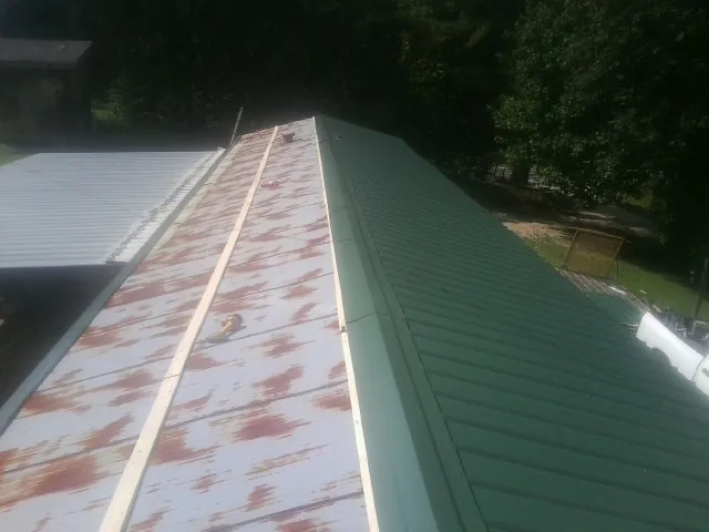 Old rusted panels beside newly installed green metal roofing — Wind Damage Roof Repair by Roofing Brothers in Pfafftown