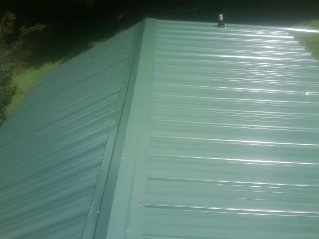 New green metal panels meeting at the ridge of a roof — Flat Roof Repair work by our crew in Pfafftown