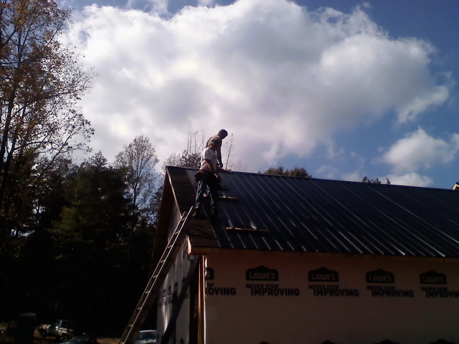 Roofer fastening dark metal panels high against a cloudy sky, from a Roof Inspection job in Pfafftown