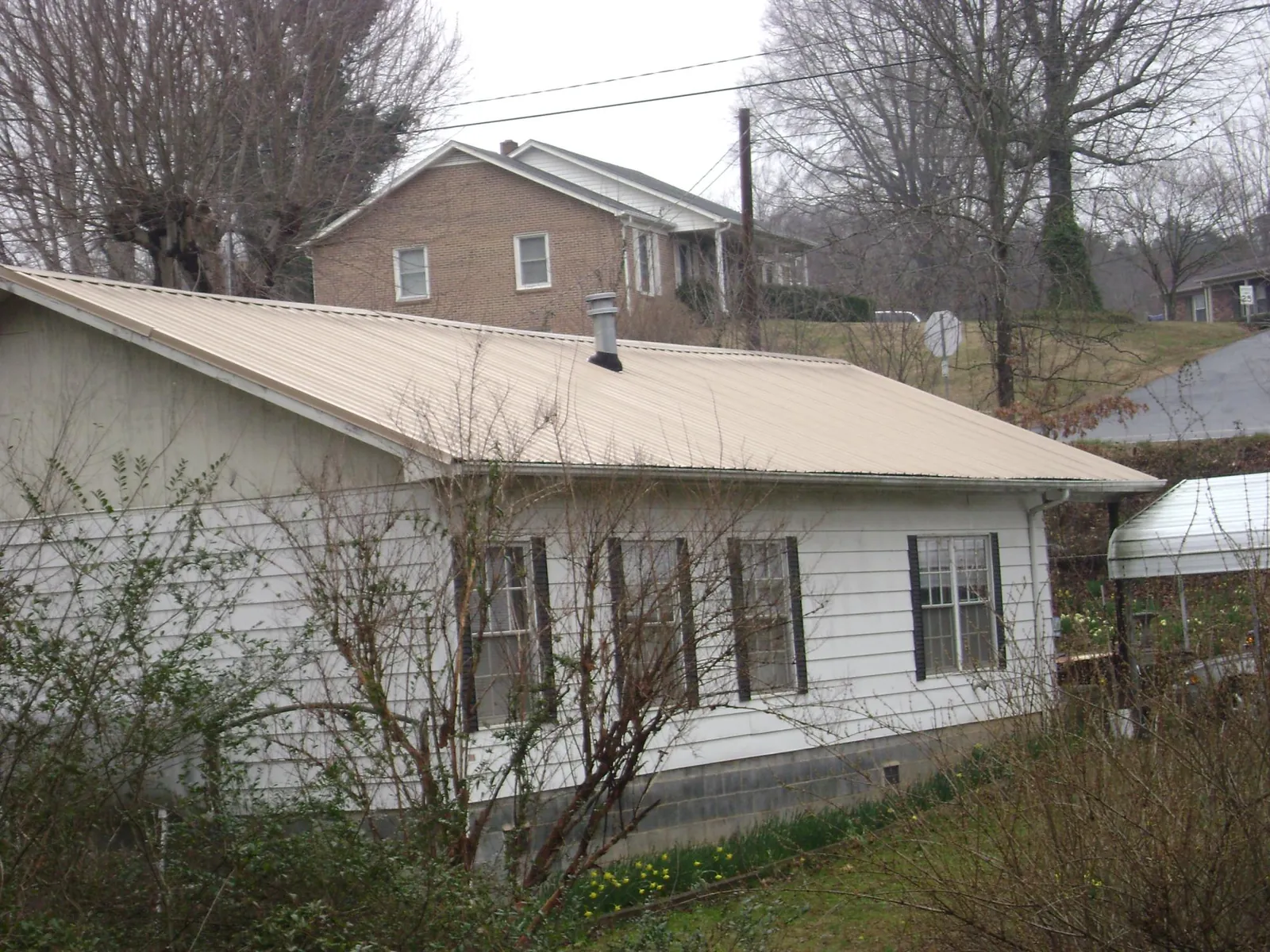 Tan metal roof on a white sided house set into a hillside — Commercial Roofing by Roofing Brothers in Pfafftown