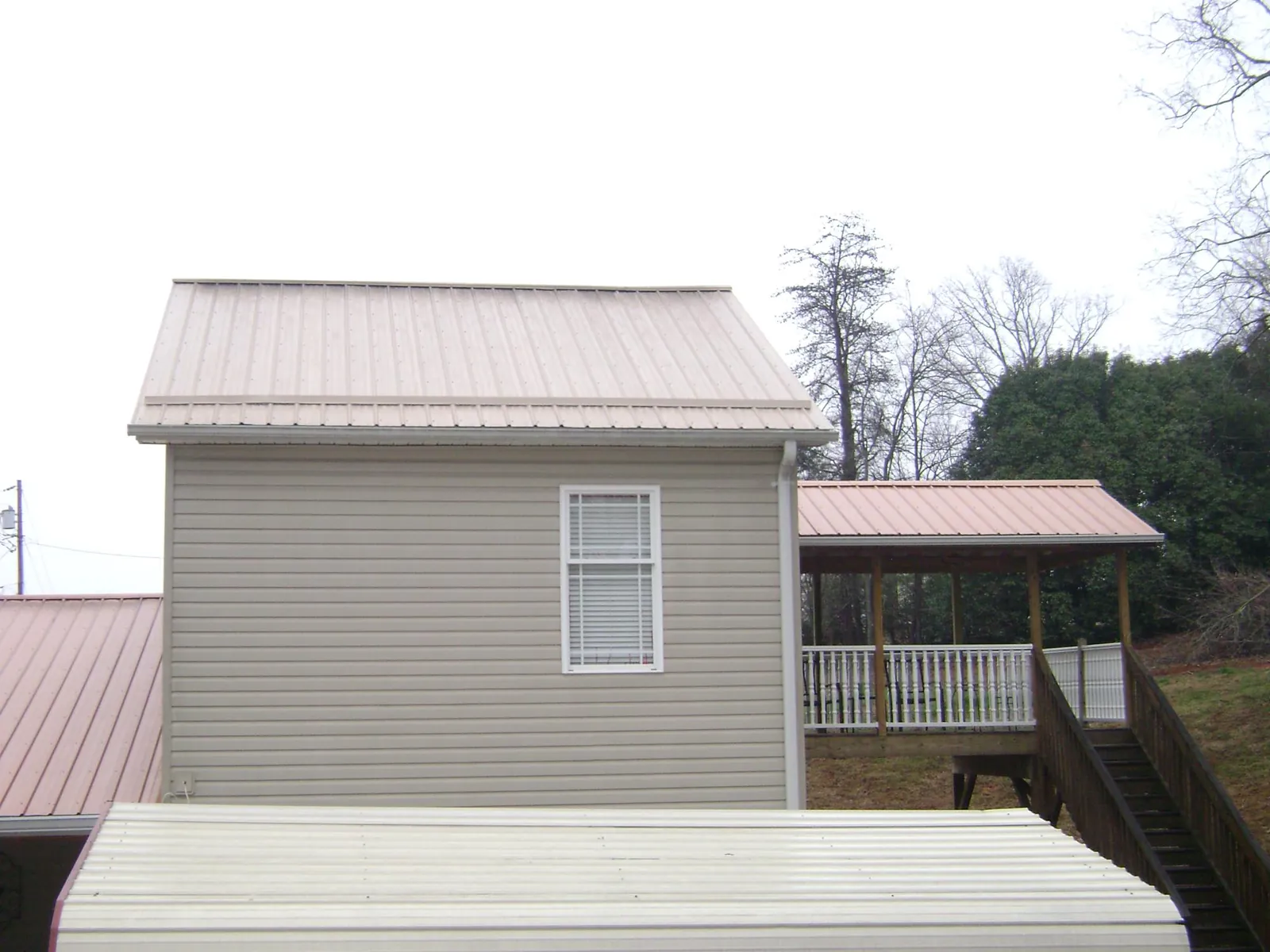 Tan metal roofs on a two story addition and attached porch, from a Roof Replacement job in Pfafftown